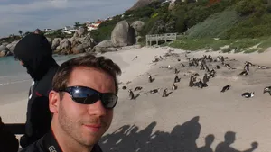 Autor am Meer in Südafrika mit Pinguinen am Strand im Hintergrund